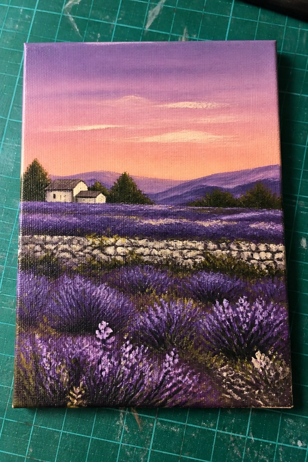 Lavender field painting with purple blooms, stone wall, houses under pink sunset sky