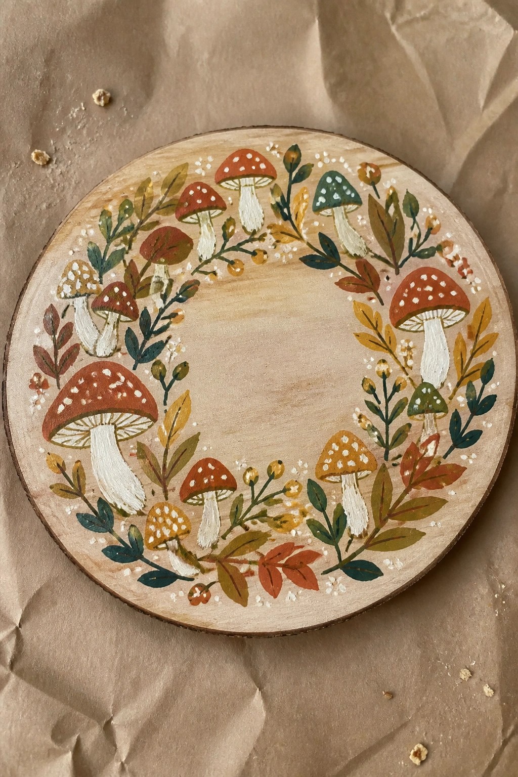 Circular wooden plaque with colorful painted mushroom and leaf wreath on brown paper