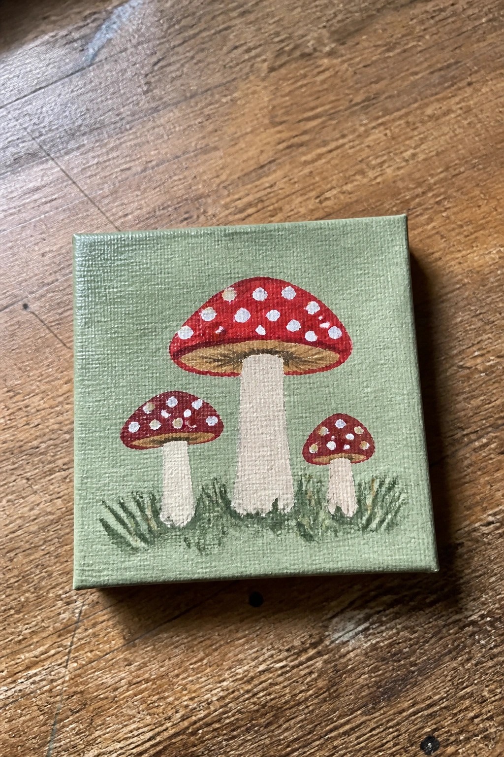 Three red spotted mushrooms with white stems on green canvas with grass