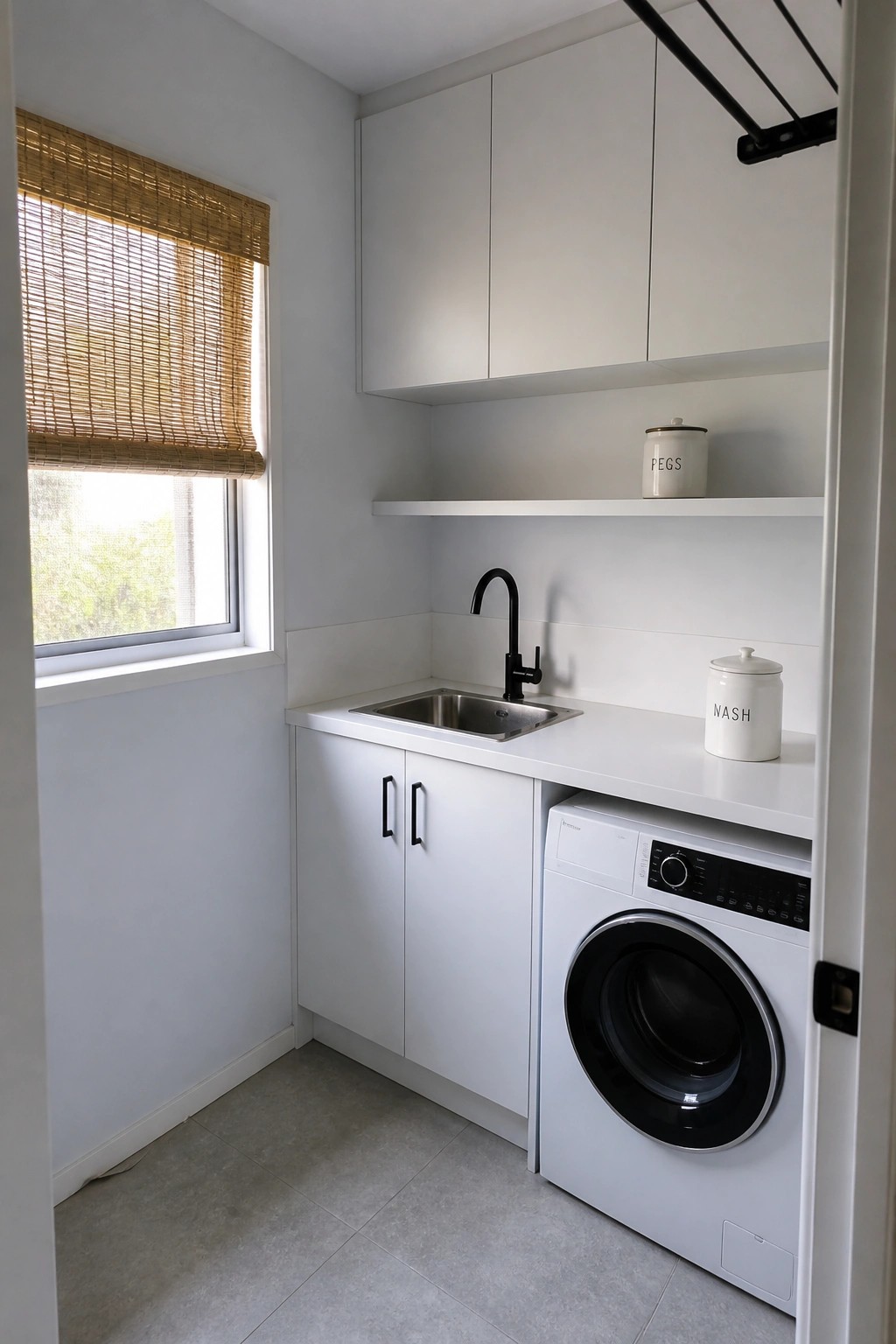Compact white laundry room with sink, washing machine, and bamboo window blind.