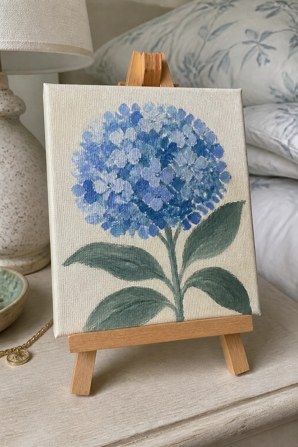 Blue hydrangea flower painting on small canvas with wooden easel and green leaves