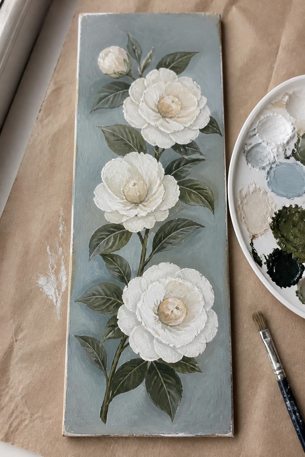 Three white flowers on blue canvas beside paint palette and brush
