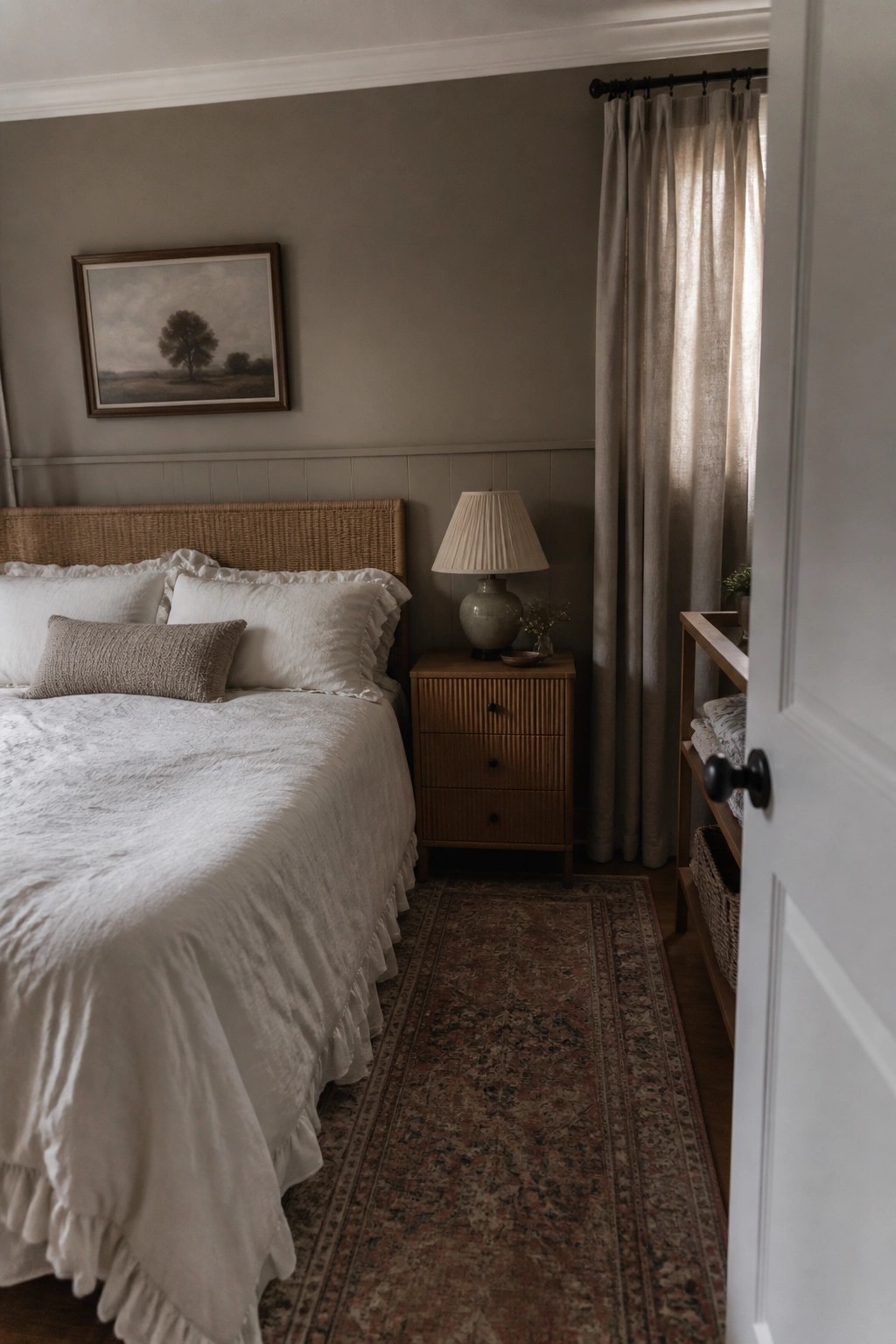 A muted greige bedroom wall painted above white paneling with a wooden headboard nearby.