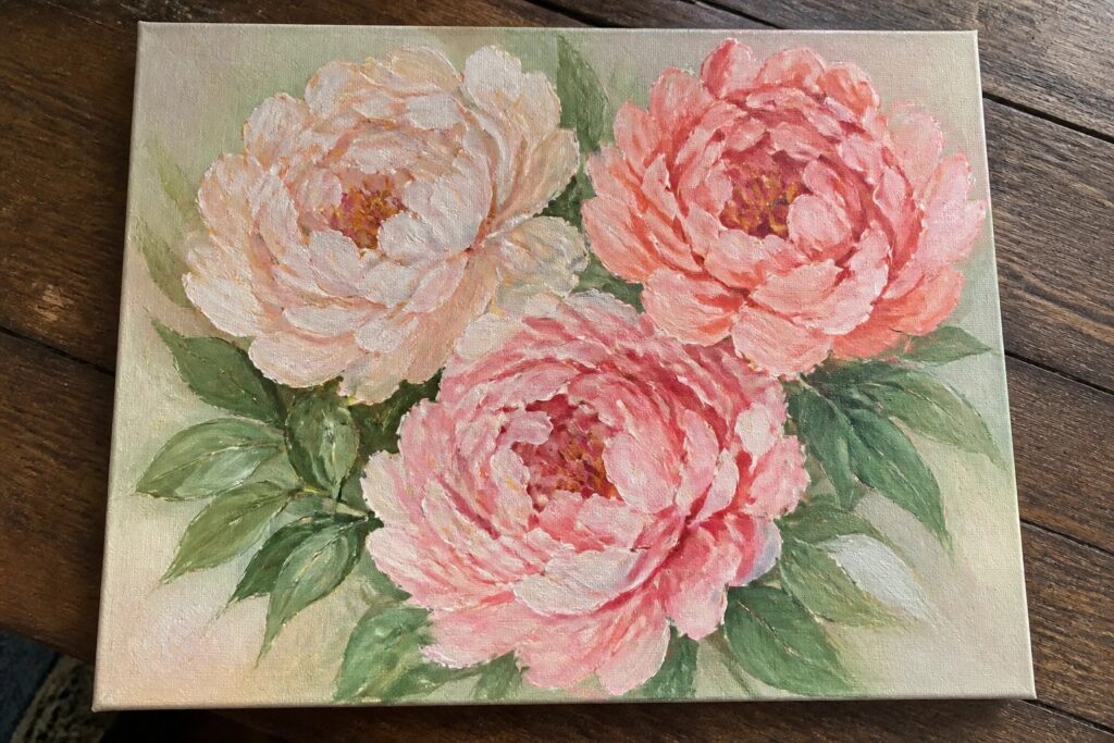 Painting of three peonies in pink, coral, and white with green leaves on wood