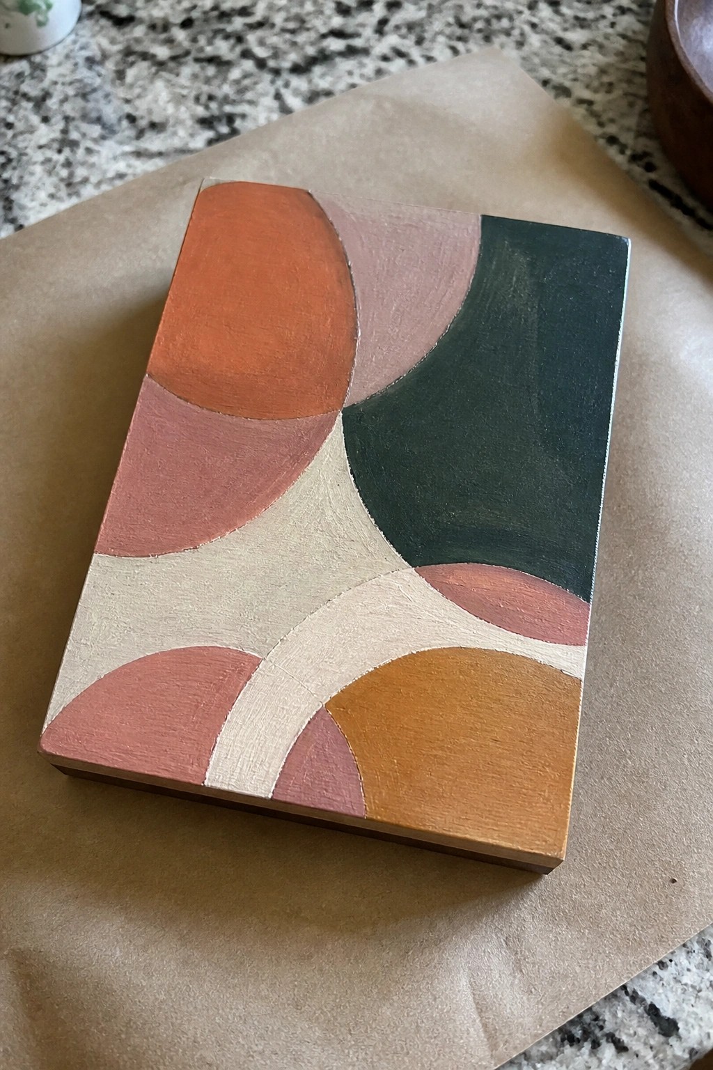 Abstract canvas with curved shapes in orange, pink, green, beige, and mustard on paper.