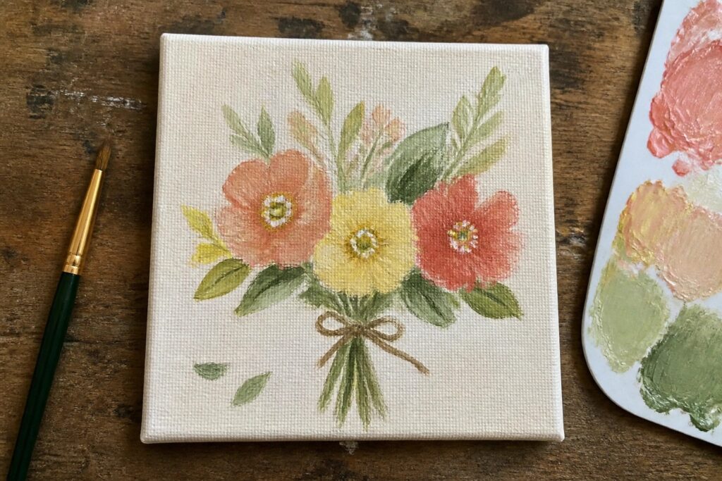 18 Small Acrylic Painting Ideas For Charming Mini Masterpieces Small canvas with pink, coral, yellow flowers and green leaves tied by bow on wood.