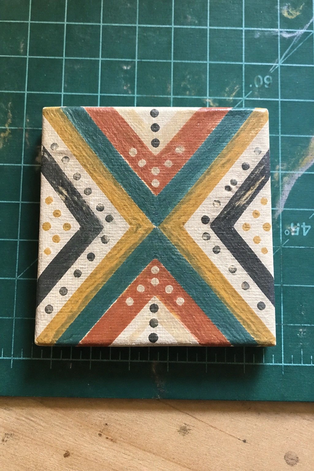 Small painted canvas with colorful chevron stripes and dotted accents on green mat