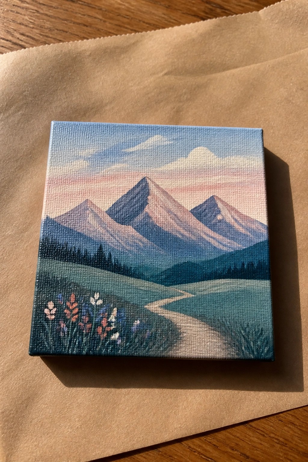 Mini canvas painting of mountains, winding path, and colorful foreground wildflowers.