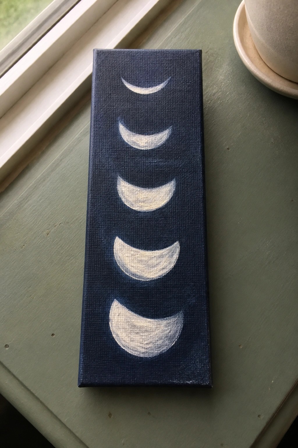 Vertical navy blue canvas with five white crescent moon phases on green table