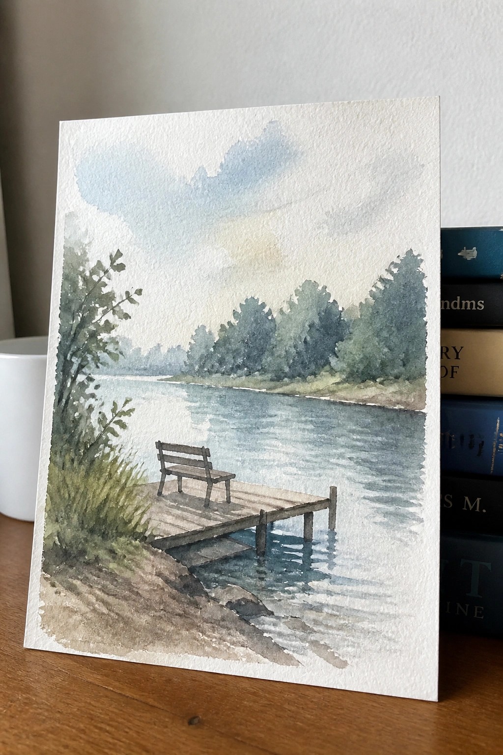 Watercolor of bench on wooden dock by calm lake with trees and stacked books