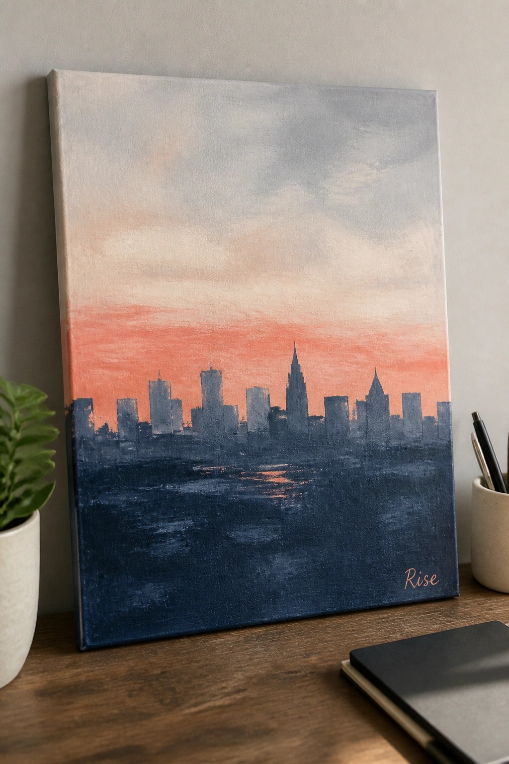 City skyline painting with orange sunset over dark blue water on wooden desk