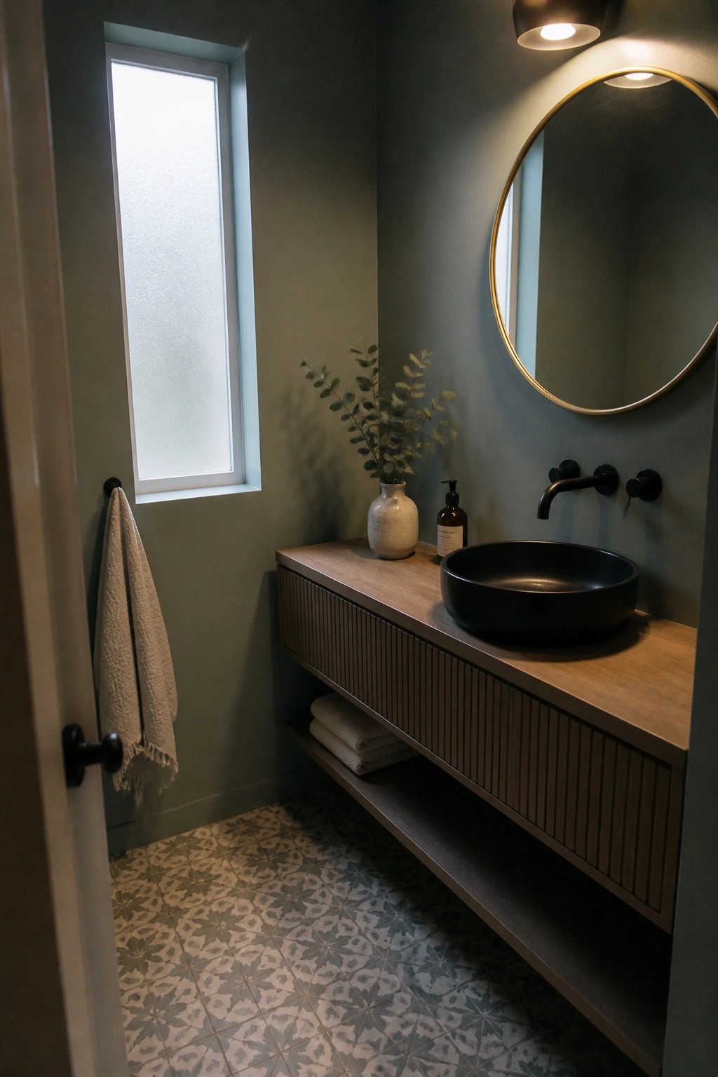 Modern bathroom with sage walls, wood vanity, black sink, gold mirror, patterned tiles.