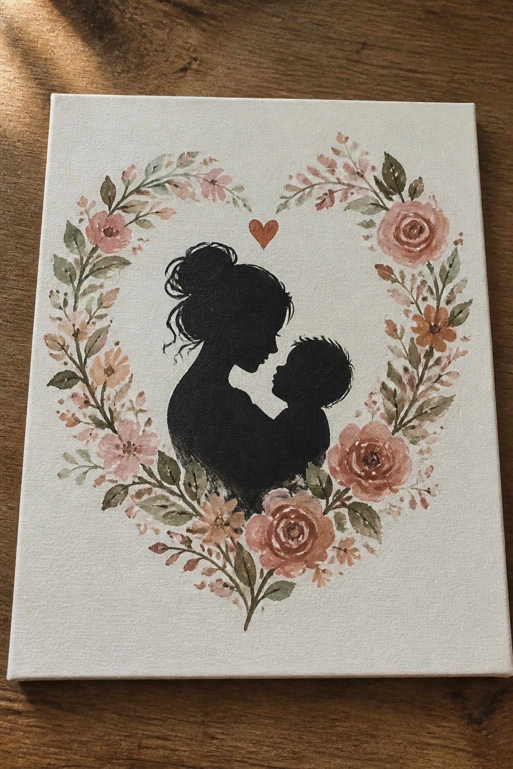 Mother and child black silhouettes embraced in a pink rose floral wreath on canvas