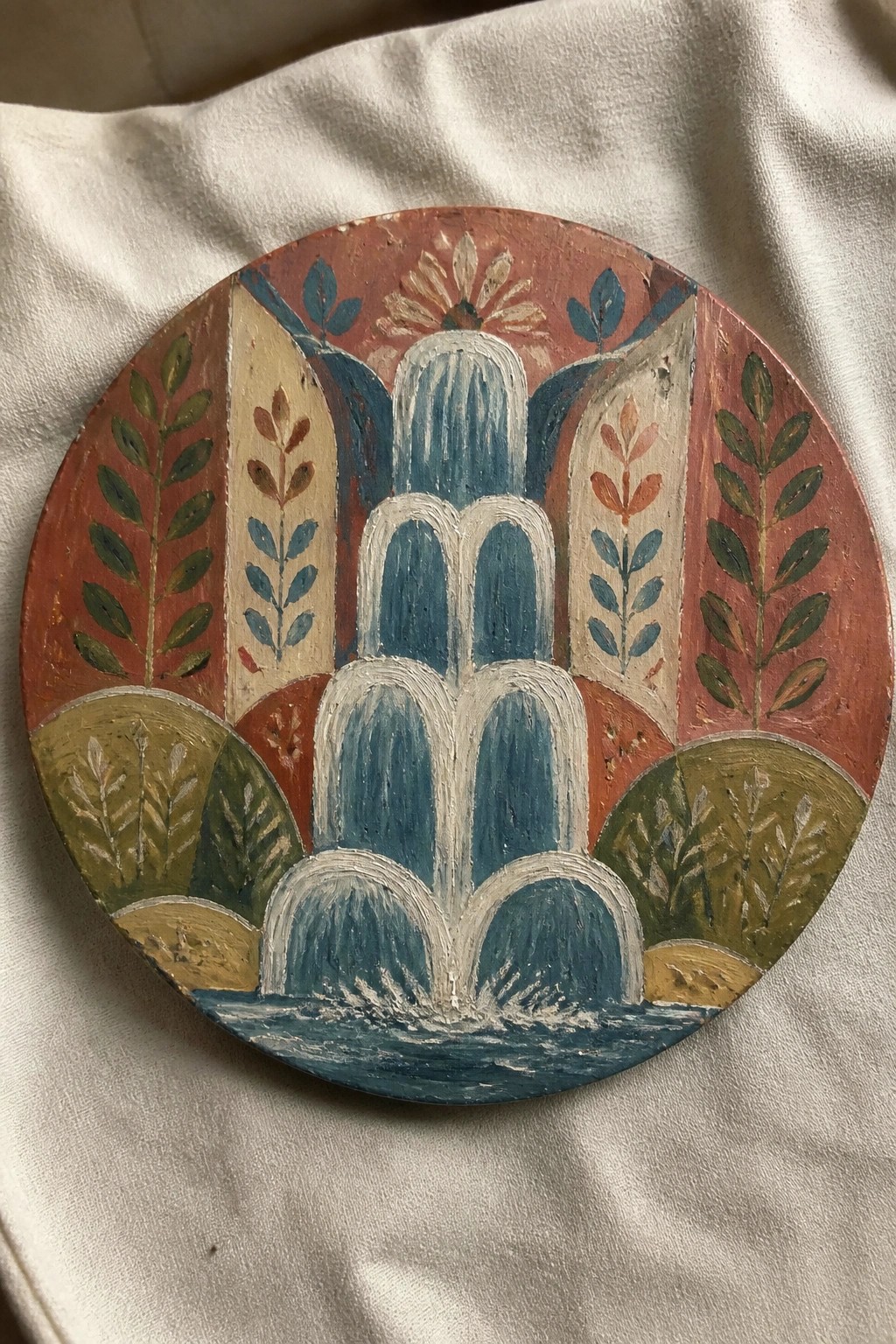 Round painted plaque of tiered blue fountain with red, green, and floral borders