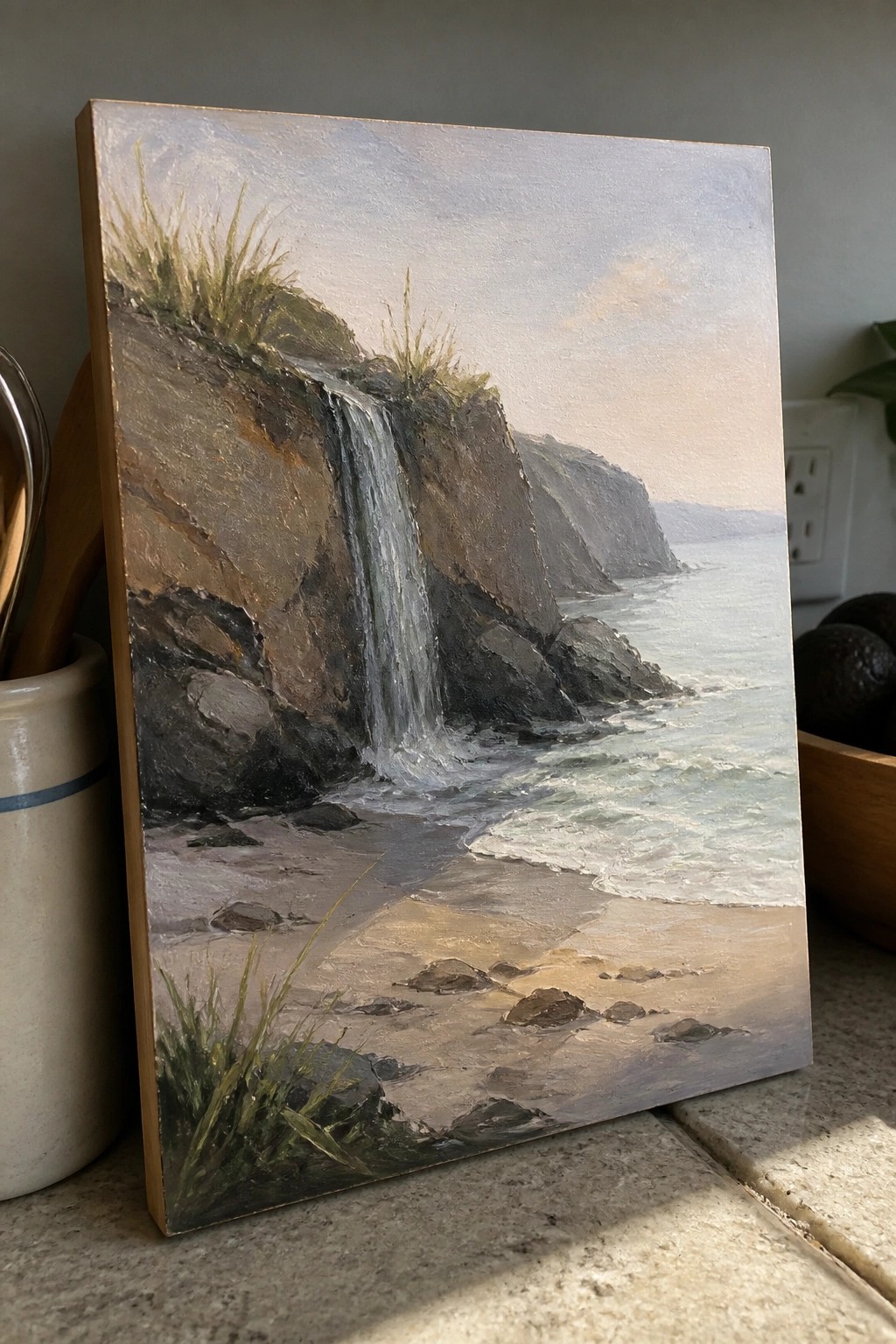 Oil painting of coastal waterfall cascading from rocky cliffs onto sandy beach with ocean waves.