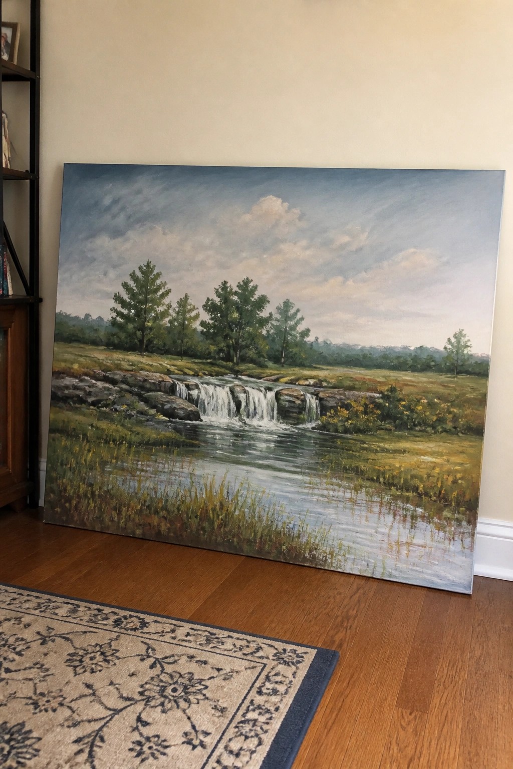 Large landscape painting of river rapids and trees leaning against wall on floor