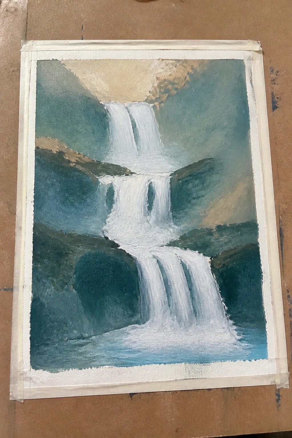 Multi-tiered white waterfall cascading over green cliffs into blue pool, taped on brown surface.