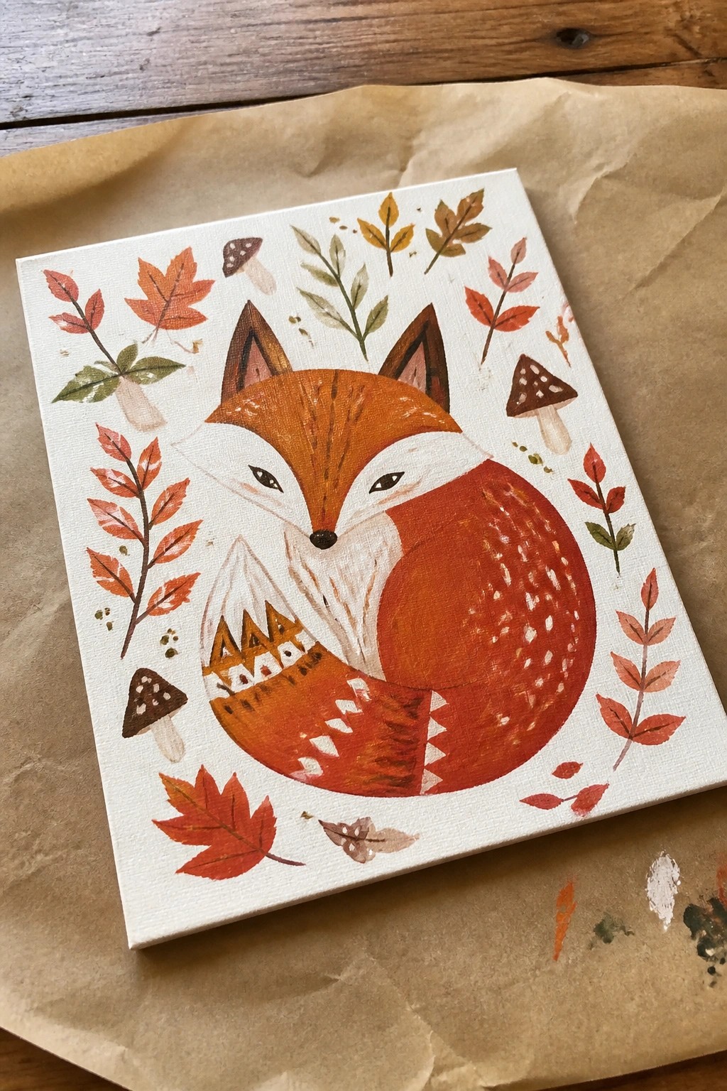 Watercolor fox curled amid autumn leaves and mushrooms on white canvas.