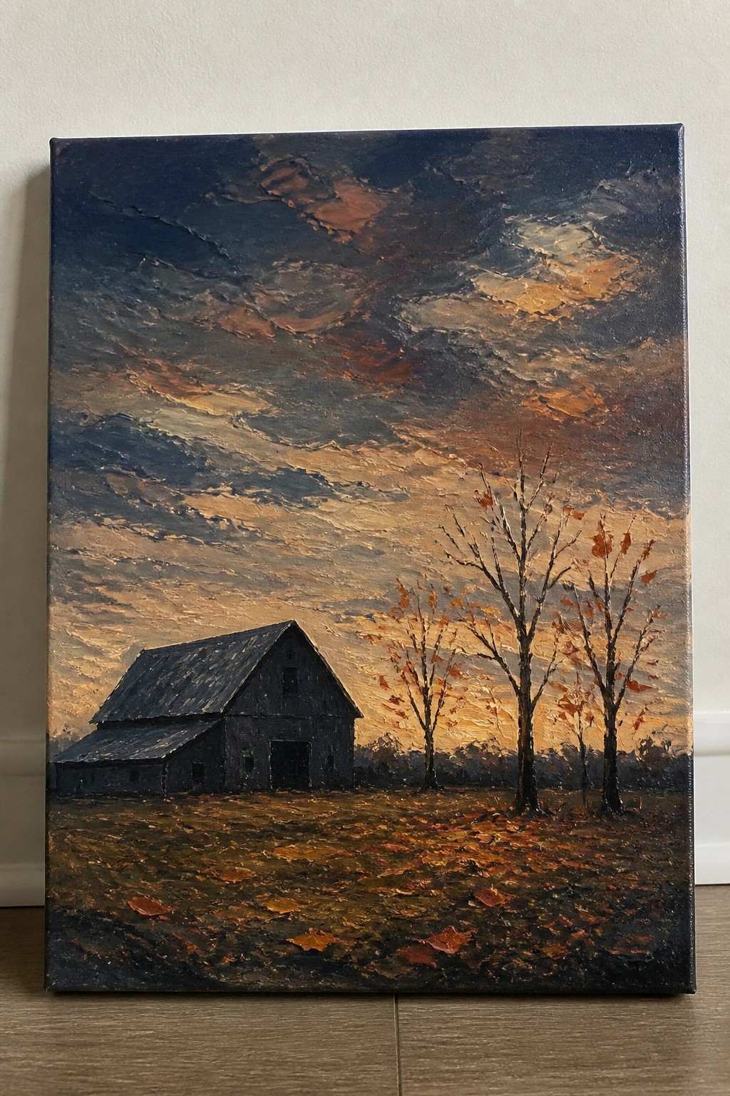 Weathered black barn in autumn field with bare trees under orange-blue sunset sky