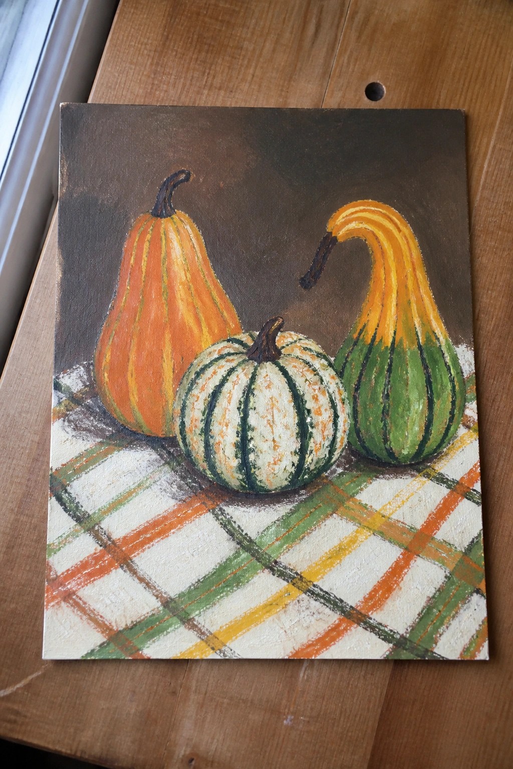 Three gourds in orange, green, and white on a plaid tablecloth.