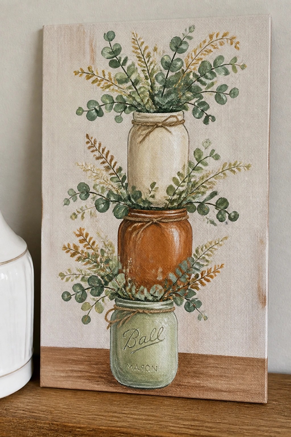 Watercolor painting of stacked green, brown, and white mason jars with greenery.
