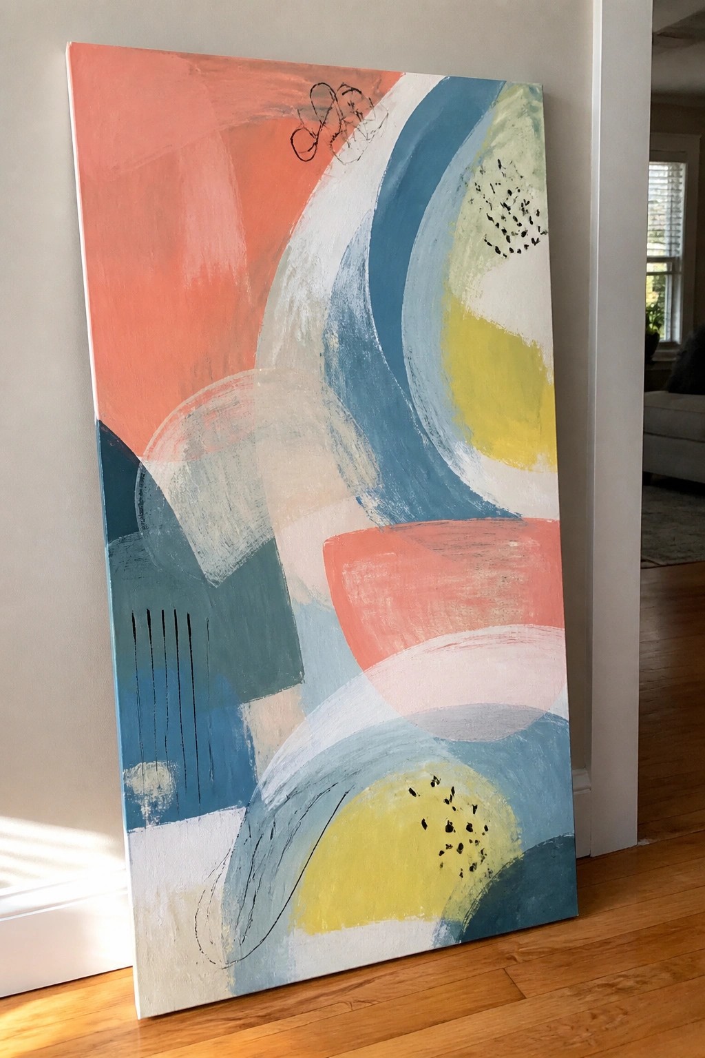 Abstract painting with coral, blue, teal, yellow curved shapes leaning on wooden floor