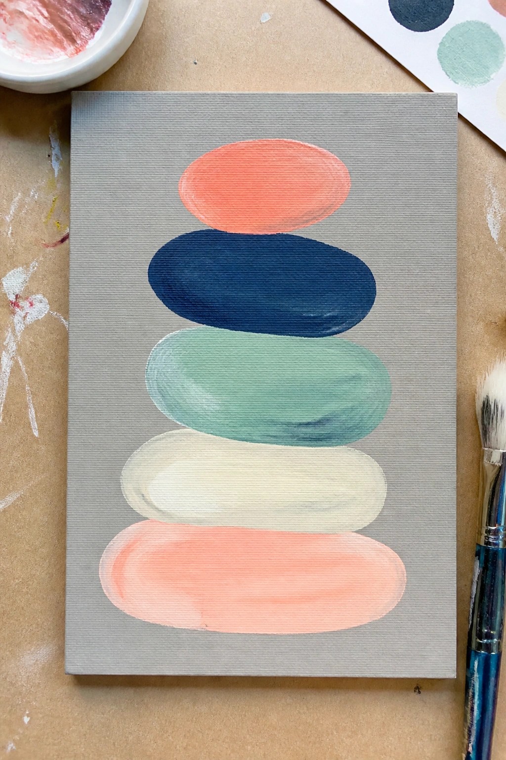 Painting of five stacked oval shapes in coral, navy, teal, cream, and coral on a gray canvas.