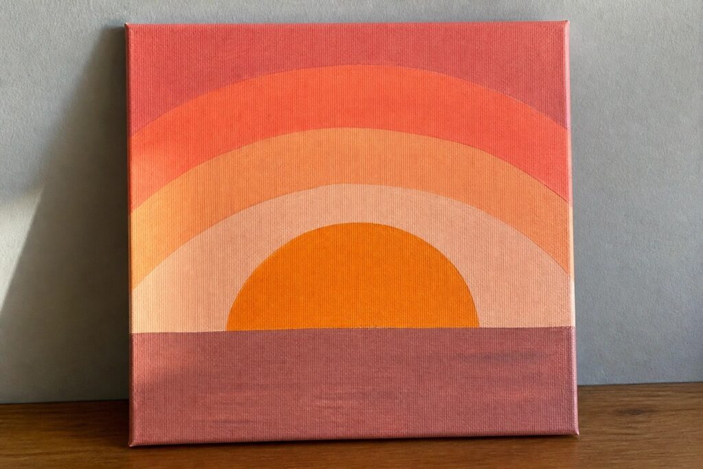 19 Beginner-Friendly Canvas Painting Ideas Using Acrylic Paint and Simple Shapes Abstract painting on canvas with orange semicircle above curved red and pink bands.
