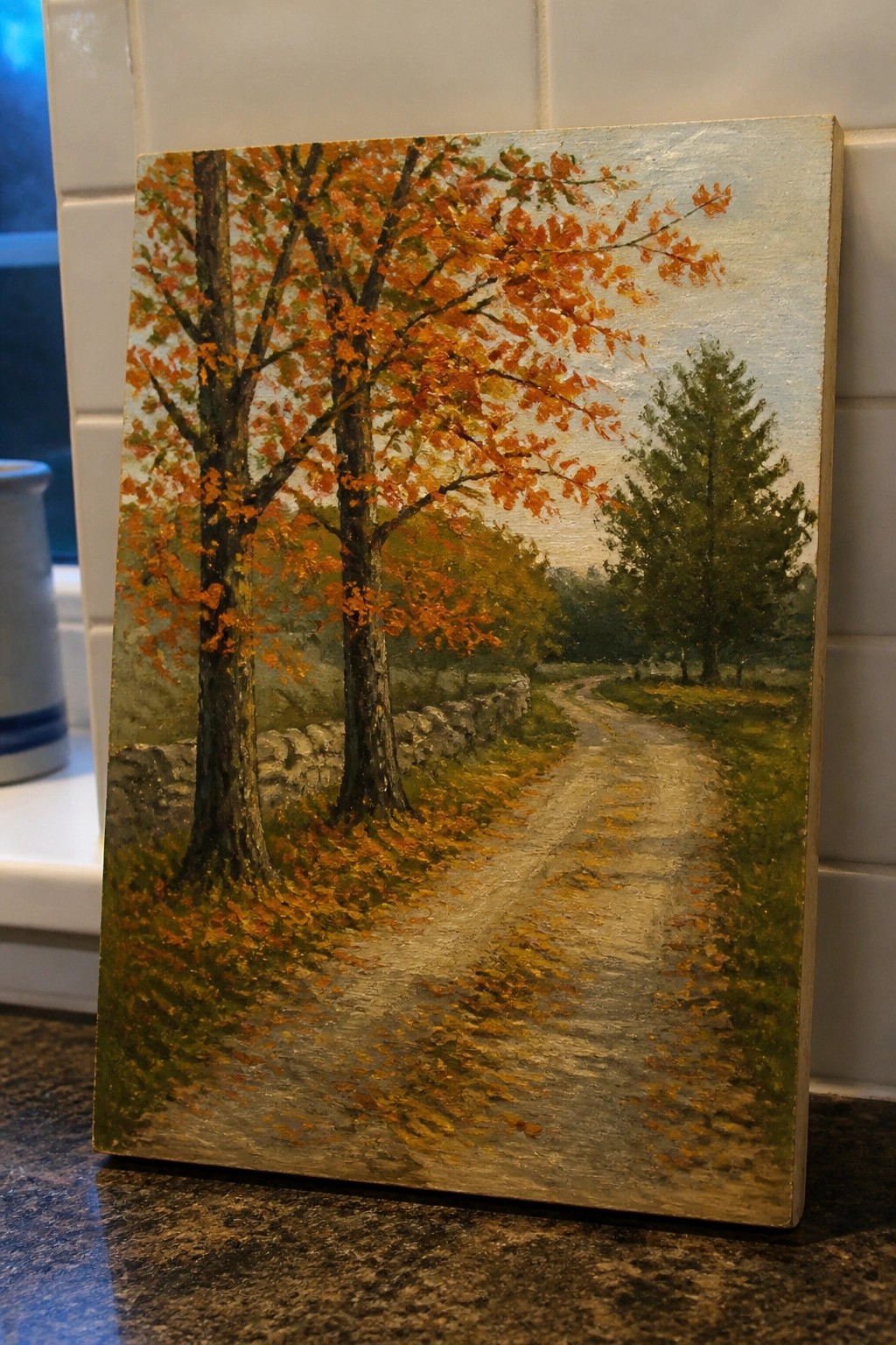 Autumn painting of orange trees beside winding dirt path on kitchen counter.