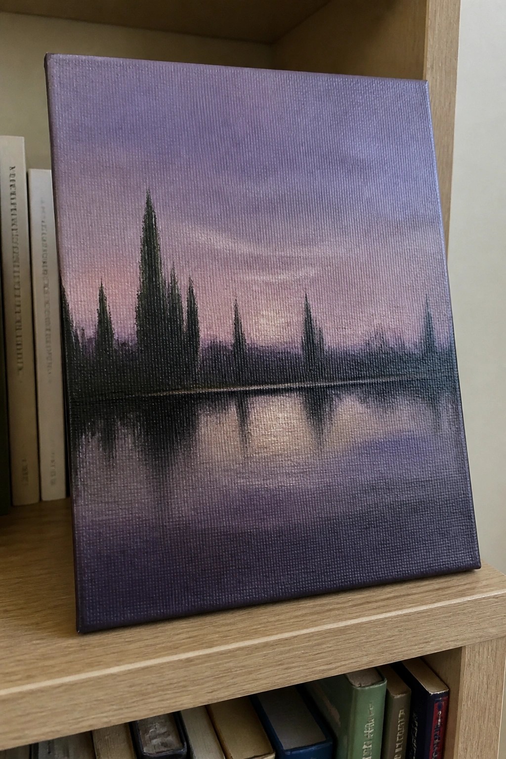 Purple-hued painting of silhouetted trees reflected in misty water on bookshelf