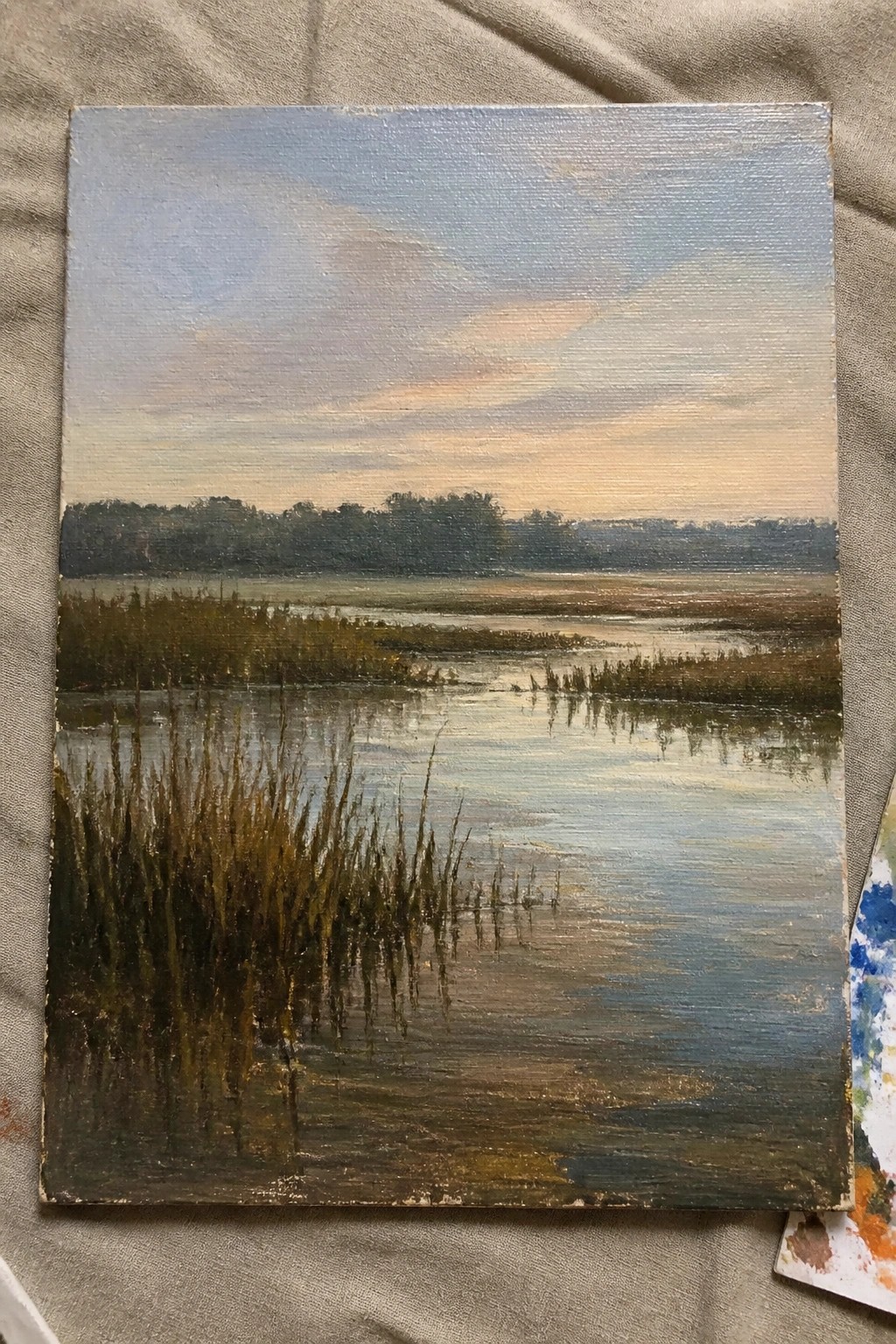 Oil painting of marsh at dusk with reflective water, golden reeds, and distant trees.