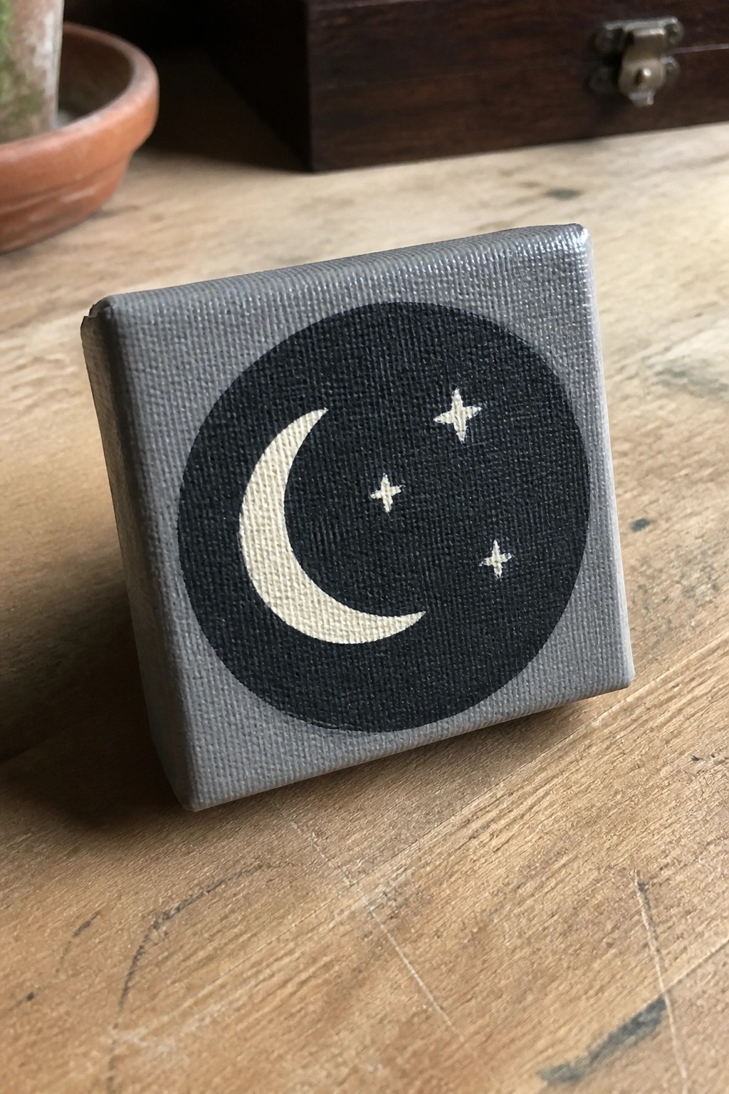 Small square canvas with black circle, white crescent moon and stars on wood