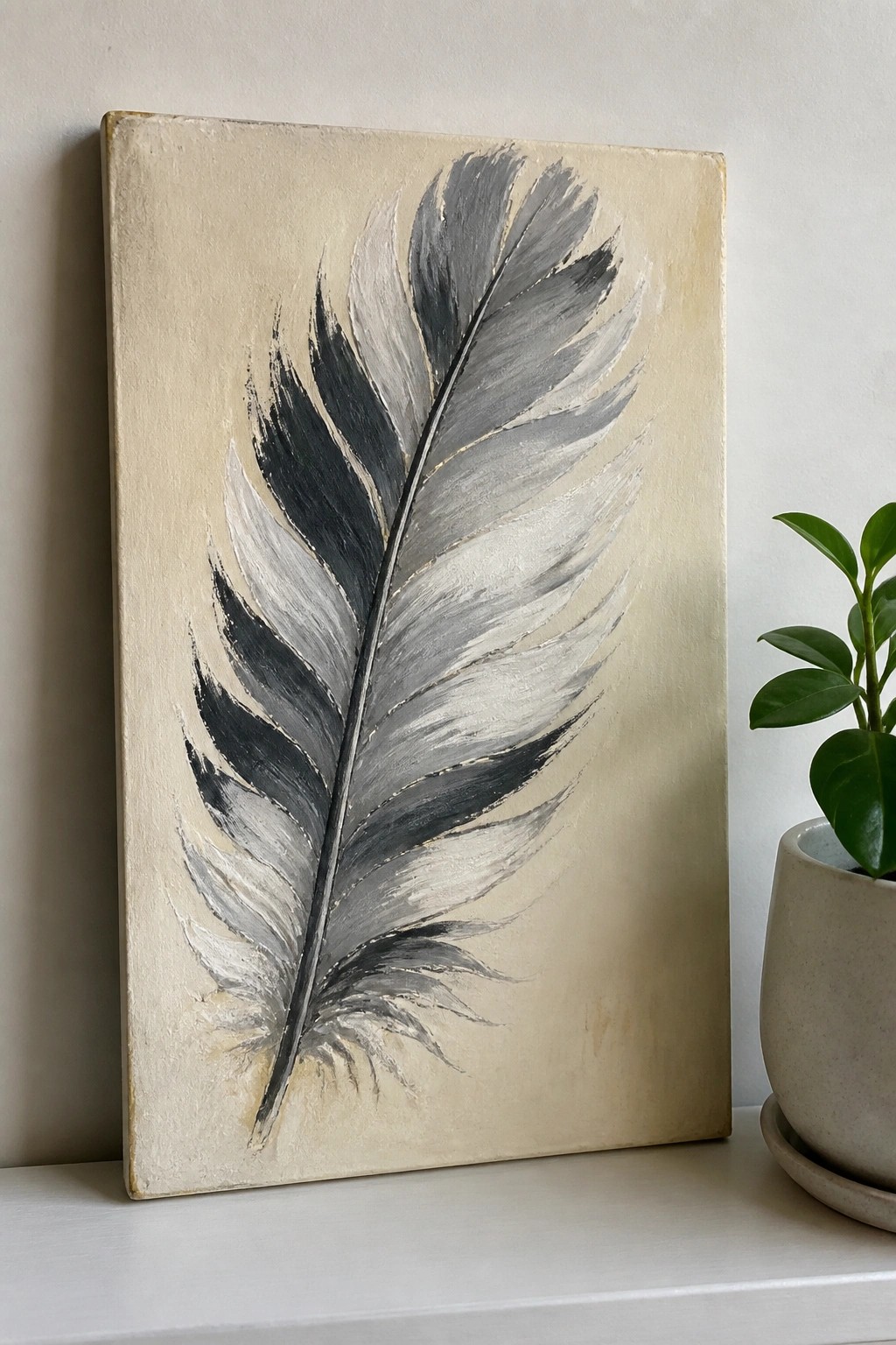 Gray feather painting with brushstrokes on beige canvas beside potted green plant.