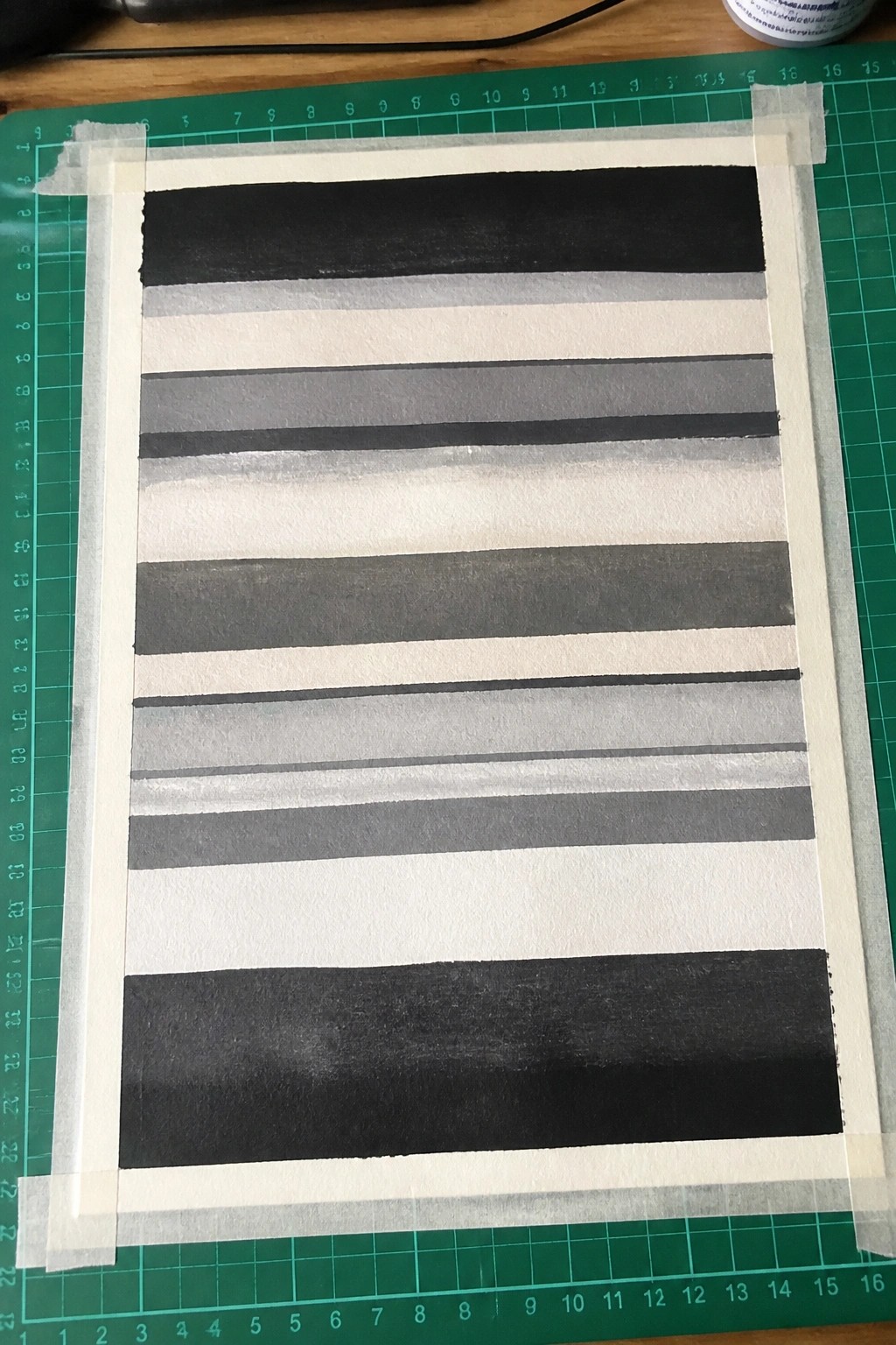 Striped black gray white painting taped on green gridded cutting mat