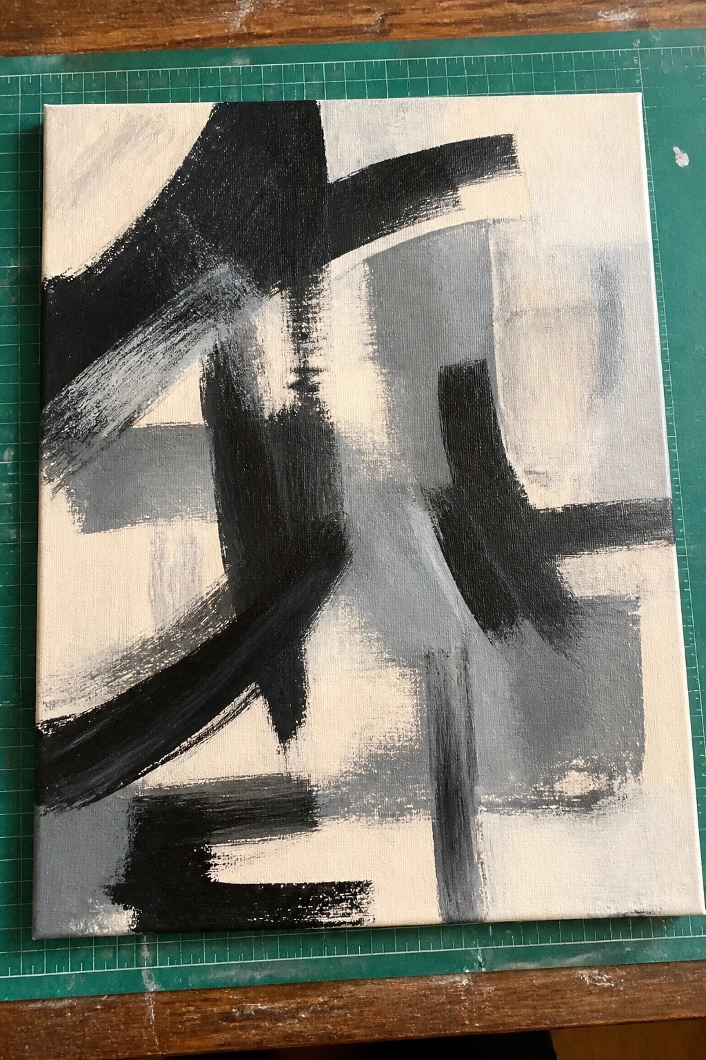 A canvas with bold black and gray abstract brushstrokes on a white background resting on a green cutting mat.