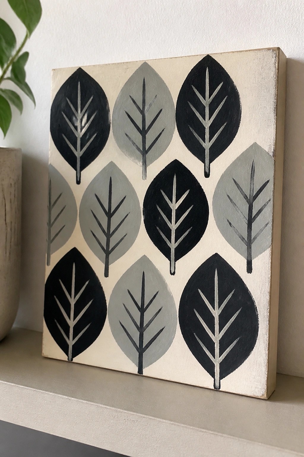 Square canvas with stylized black and gray leaves on beige background on shelf