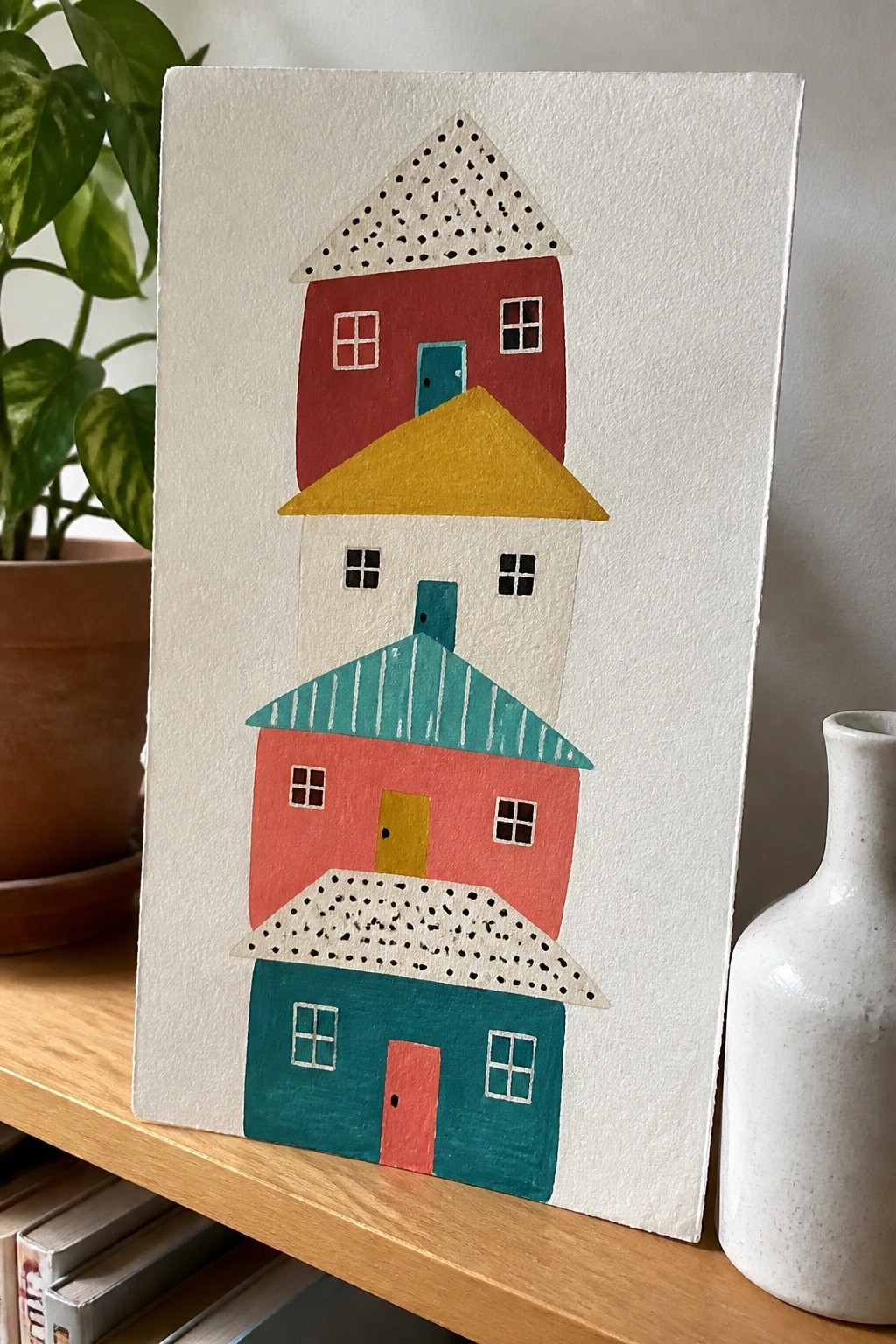 Colorful stacked houses painting on canvas beside plant and white vase
