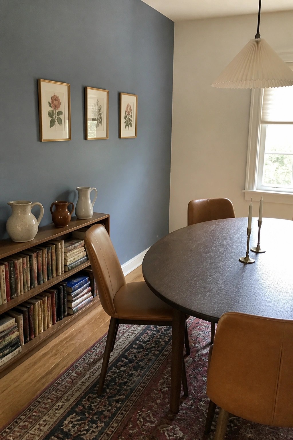 A dining room with blue-gray walls, a wooden bookshelf, and a round table on a patterned rug.