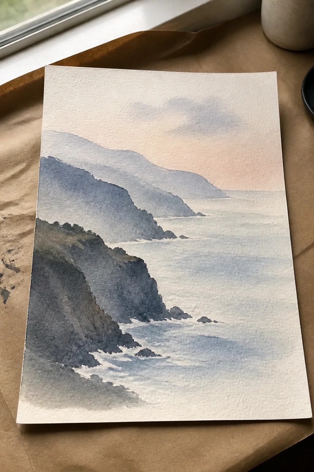 Watercolor painting of rocky cliffs by calm sea with misty mountains at dusk.