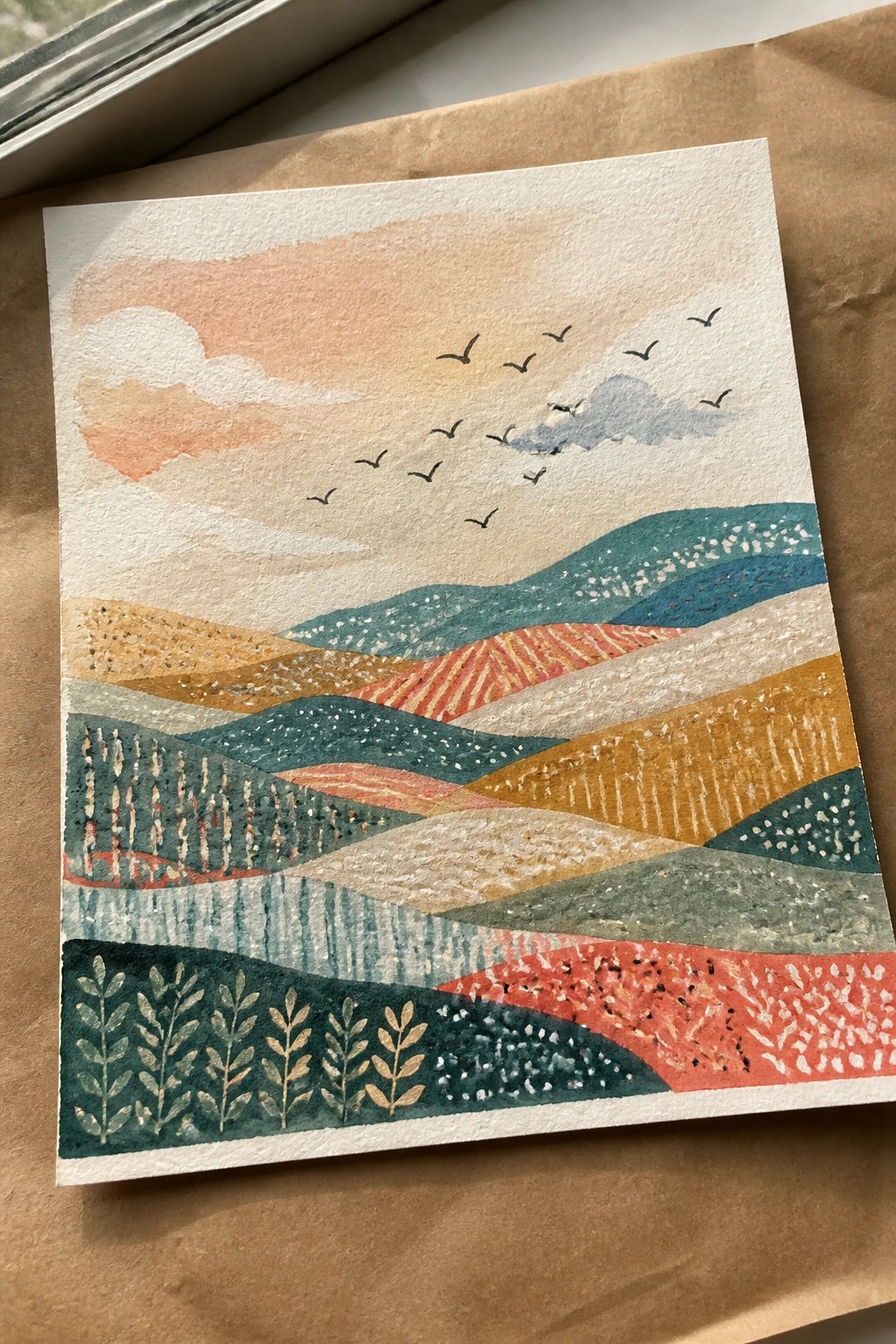 Watercolor landscape of patterned rolling hills in teal, orange, and red under a peach sky with birds