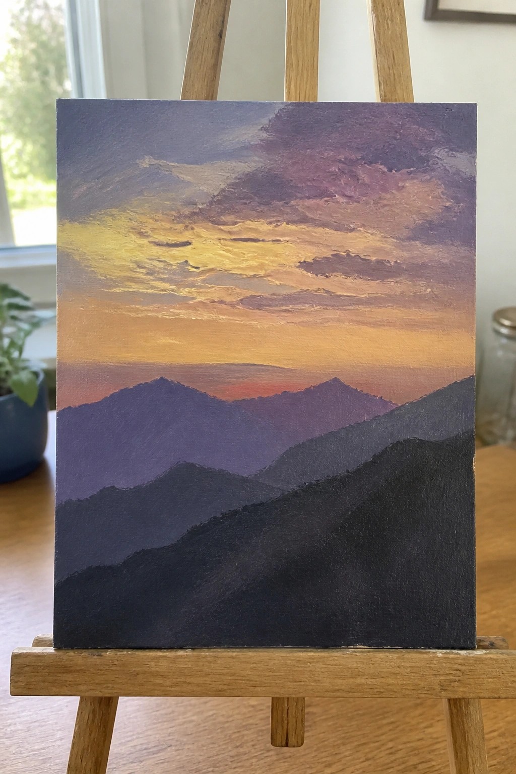 Canvas on easel with silhouetted mountains under vibrant orange-purple sunset sky