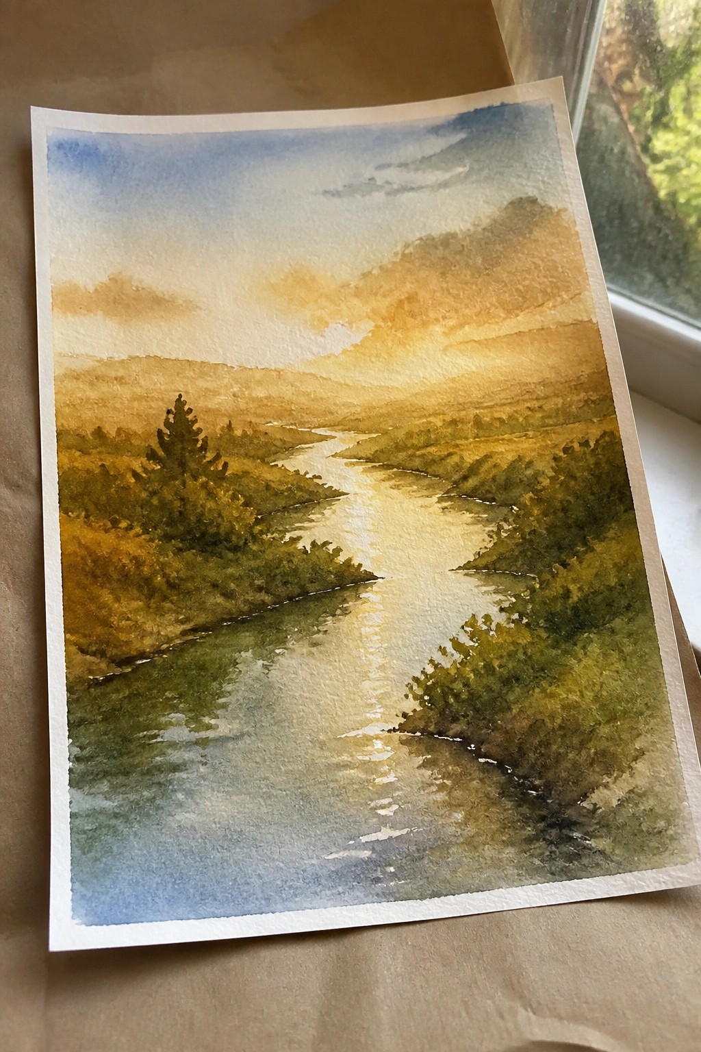 Watercolor landscape of winding river reflecting sunset light between green hills.