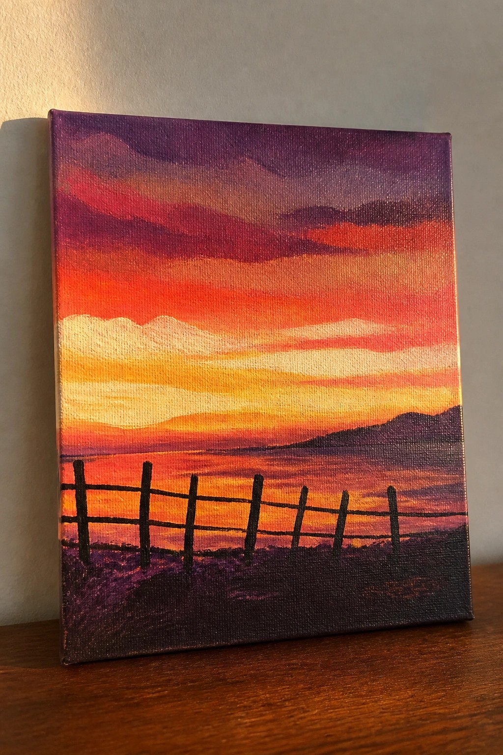 Vibrant sunset painting with fiery orange skies, purple clouds, and silhouetted fence.
