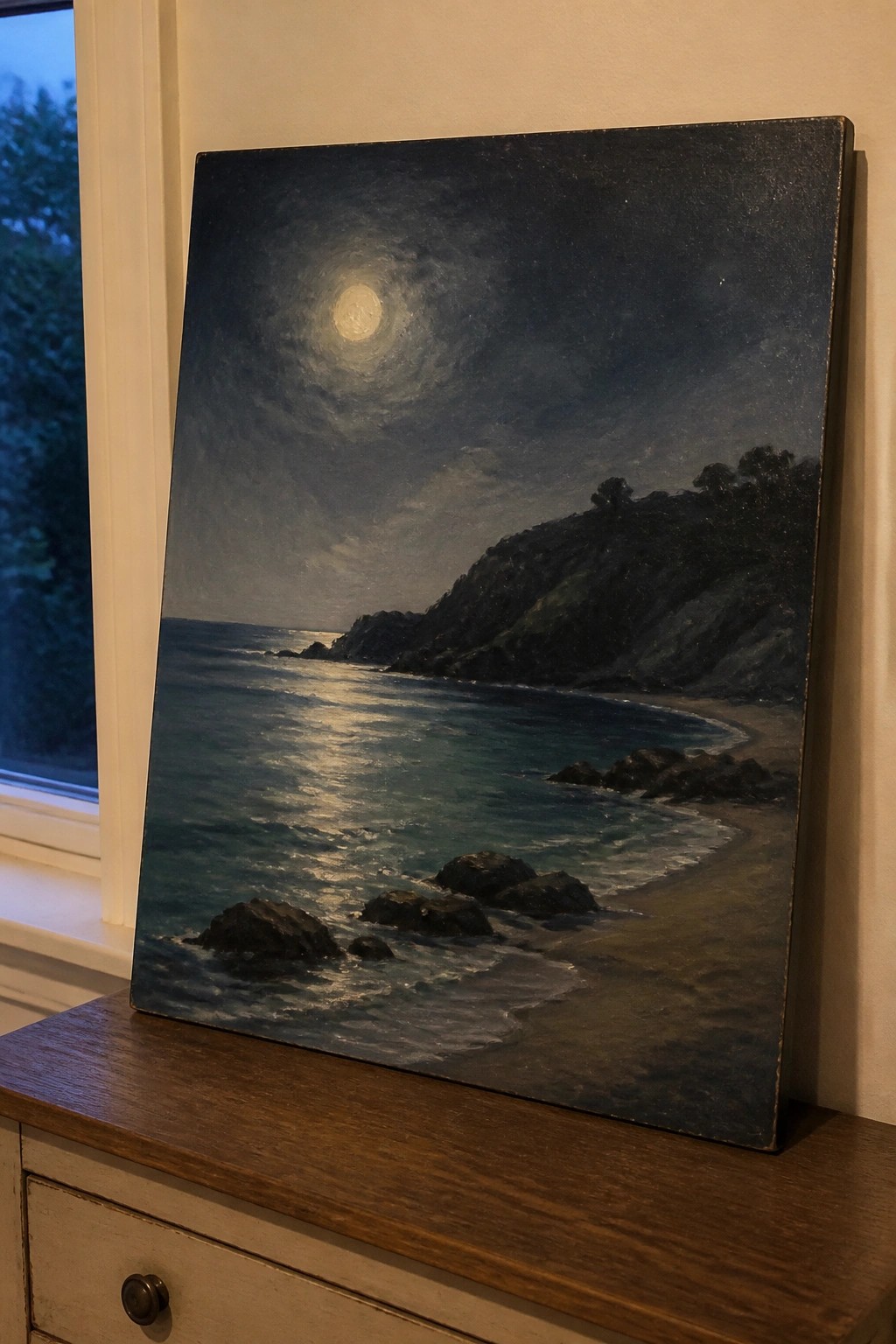 Moonlit seascape painting with waves on rocky shore leaning on wooden dresser