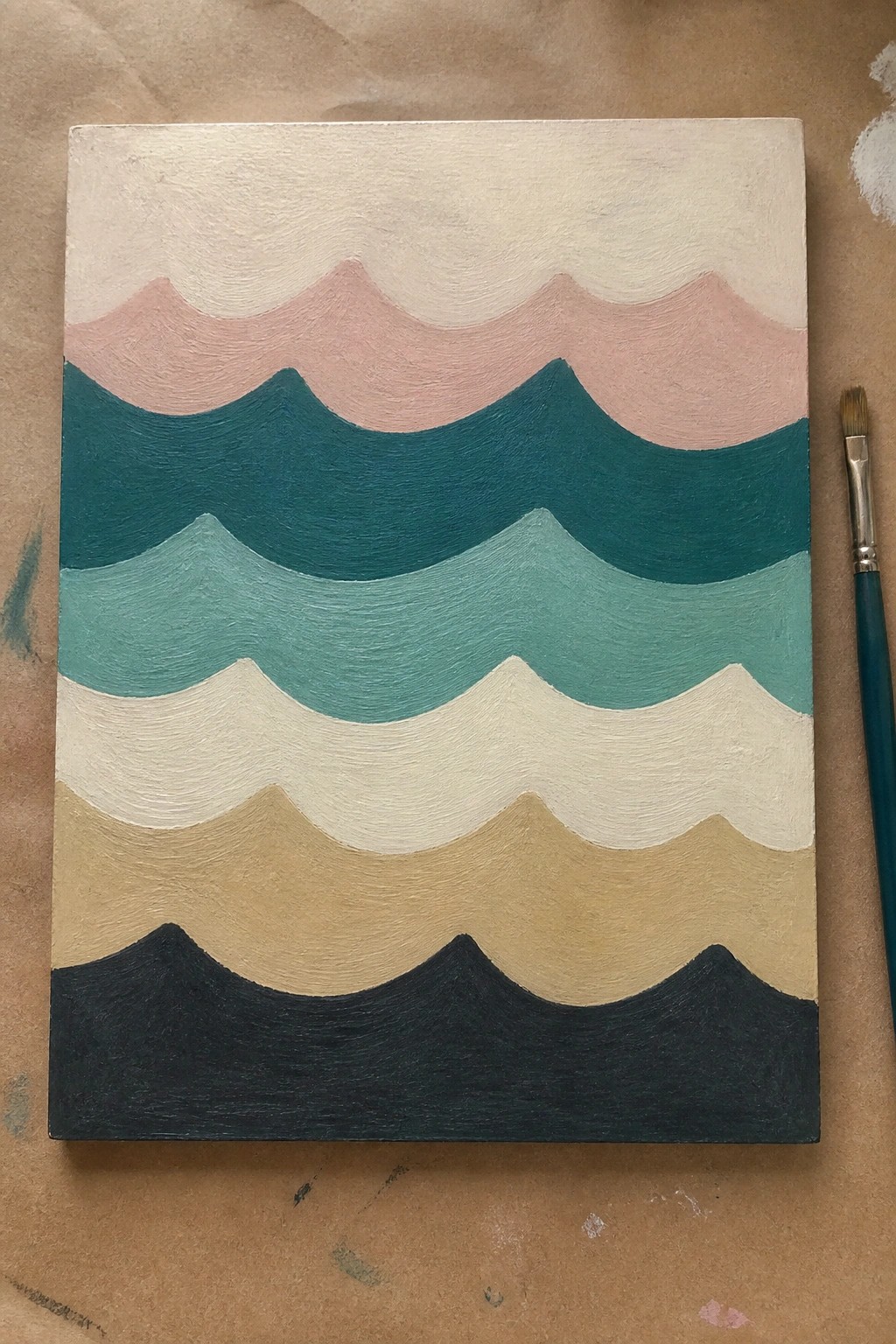 Abstract wave painting with pink, teal, beige, and black stripes on canvas beside brush