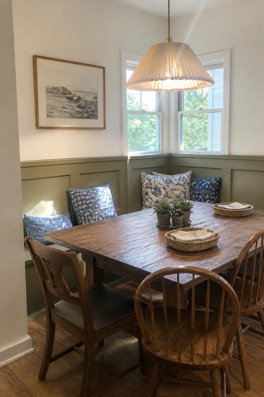 Muted green wainscoting lines the lower walls of a dining nook with a wooden table and chairs.