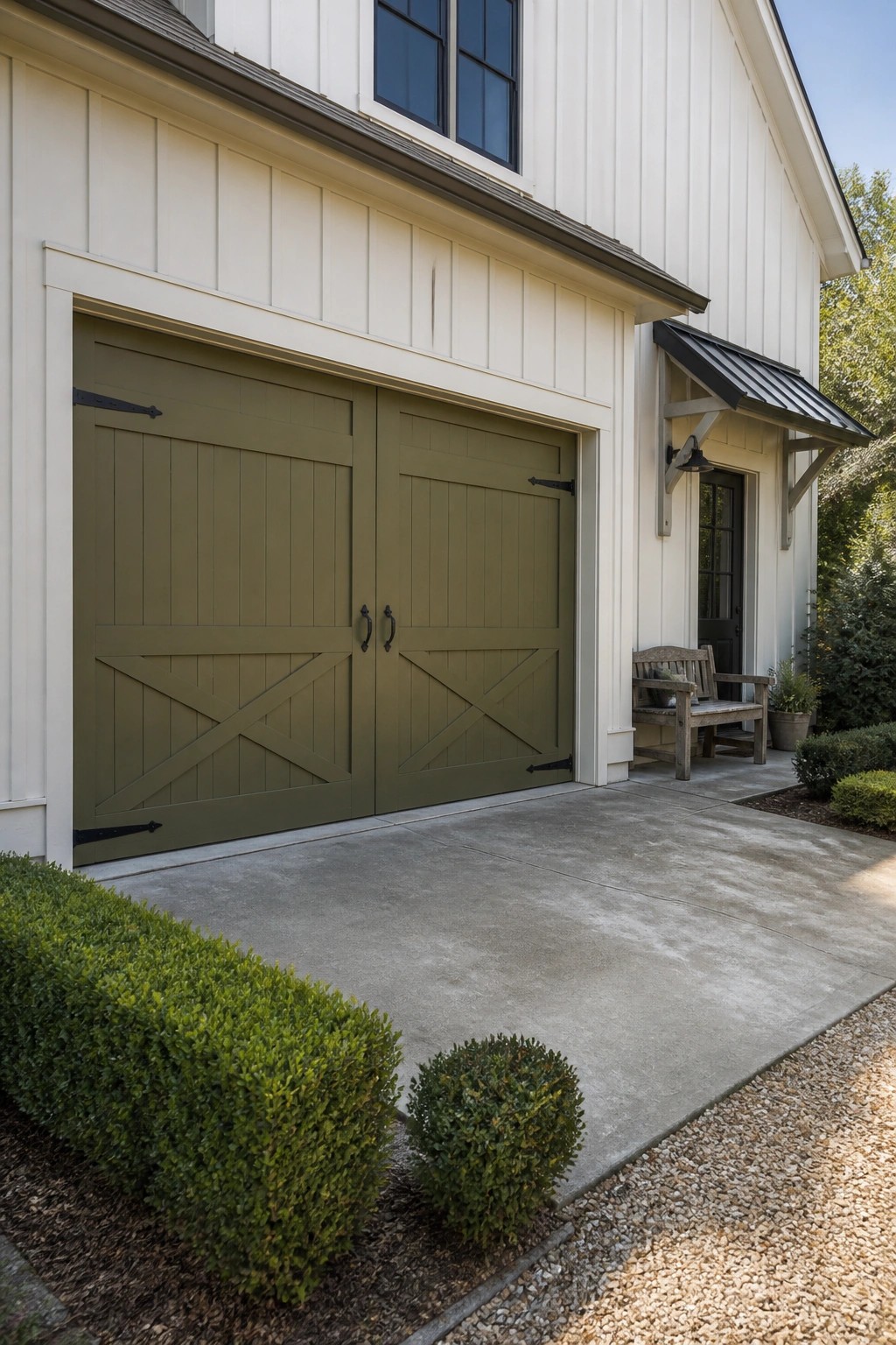 Olive green carriage-style garage doors on white house with shrubs and driveway.