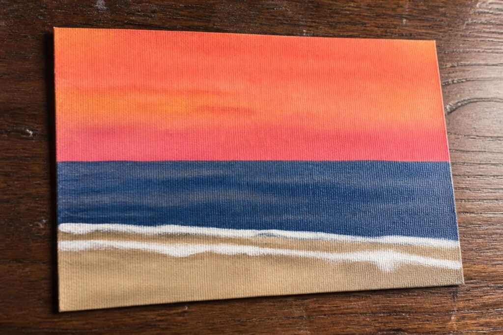 Acrylic painting of red-orange sunset over blue ocean with white waves and brown sand.
