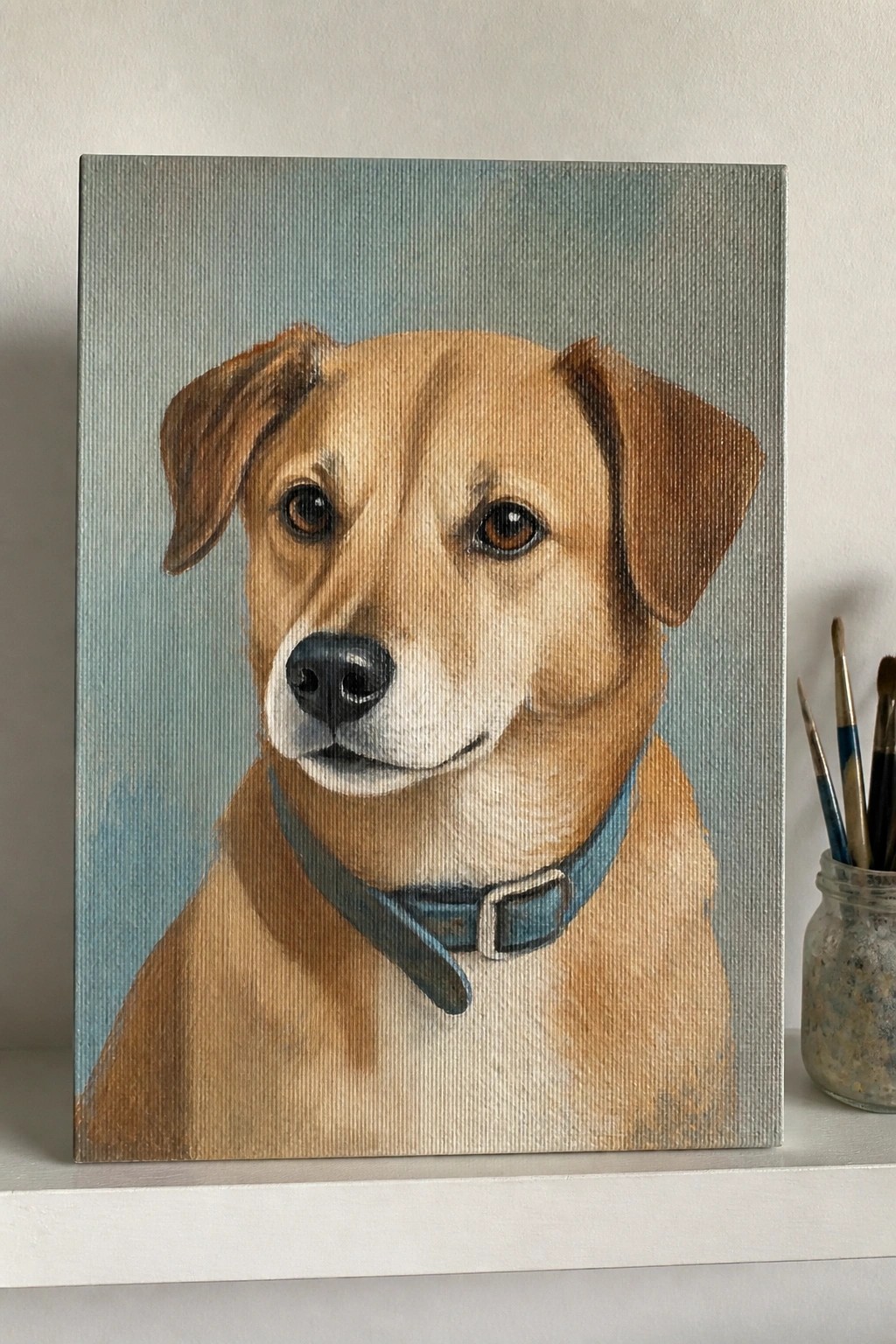 Realistic painting of tan dog with blue collar on canvas beside paintbrushes in jar
