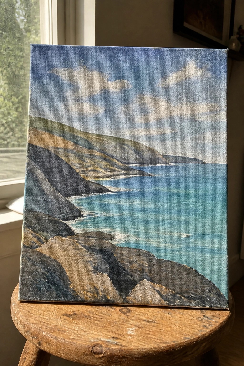 Oil painting of green cliffs by blue sea on wooden stool.